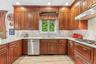 Cherry wood cabinetry, light-toned countertops, subway tile backsplash, stainless steel dishwasher, and a gas cooktop