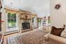 Vaulted ceiling with recessed lighting, stone fireplace with hearth and wood mantel, large pane windows, and wood-finish flooring