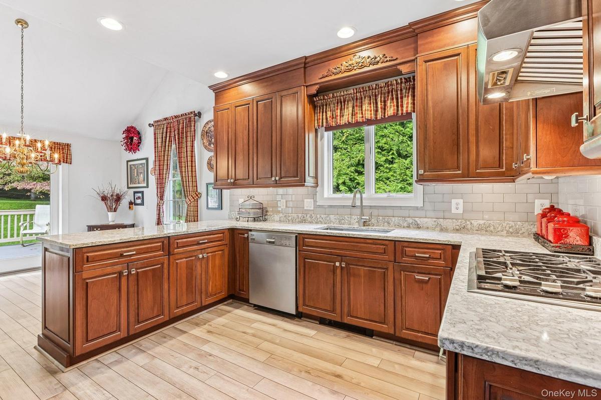 Kitchen featuring wood-finish flooring, ample wood cabinetry, light-toned countertops, a subway tile backsplash, and stainless steel appliances