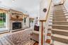 Stone-clad fireplace with a wood mantle, hardwood flooring, and a carpeted staircase with a wood handrail