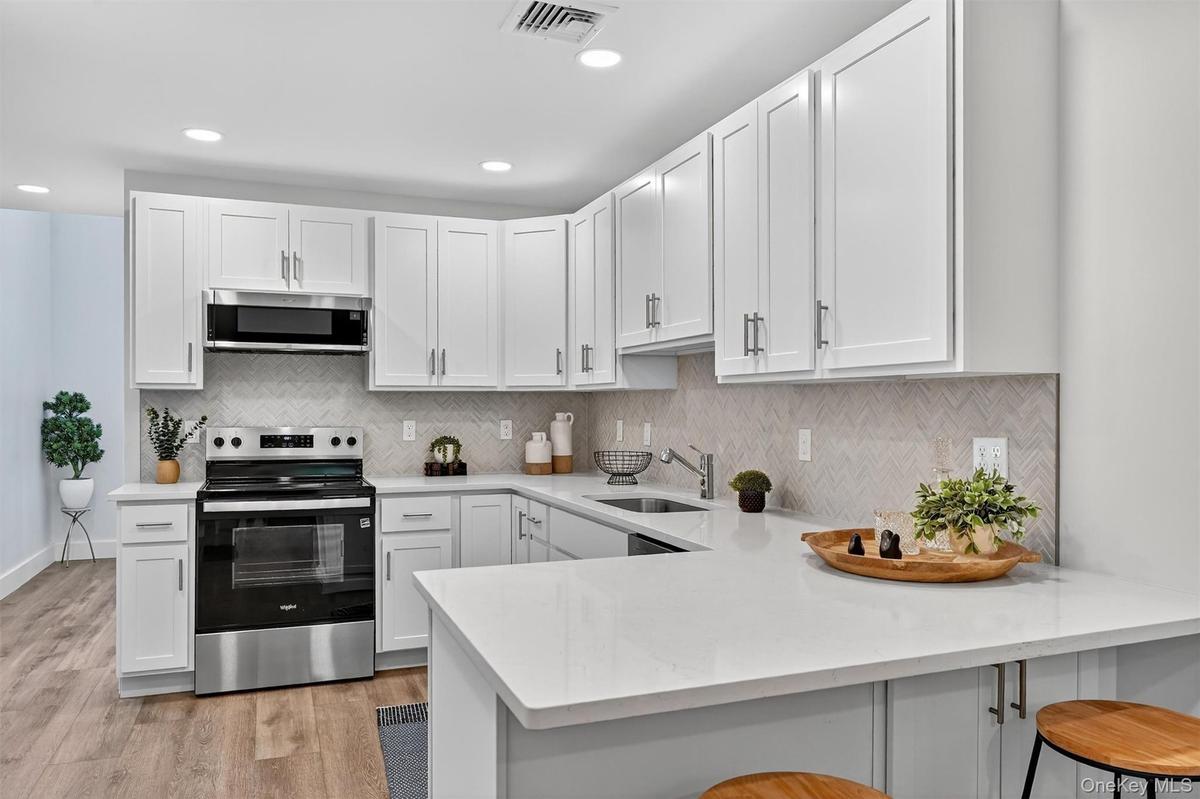 Kitchen with stainless steel appliances, white cabinets, backsplash, a breakfast bar, and recessed lighting