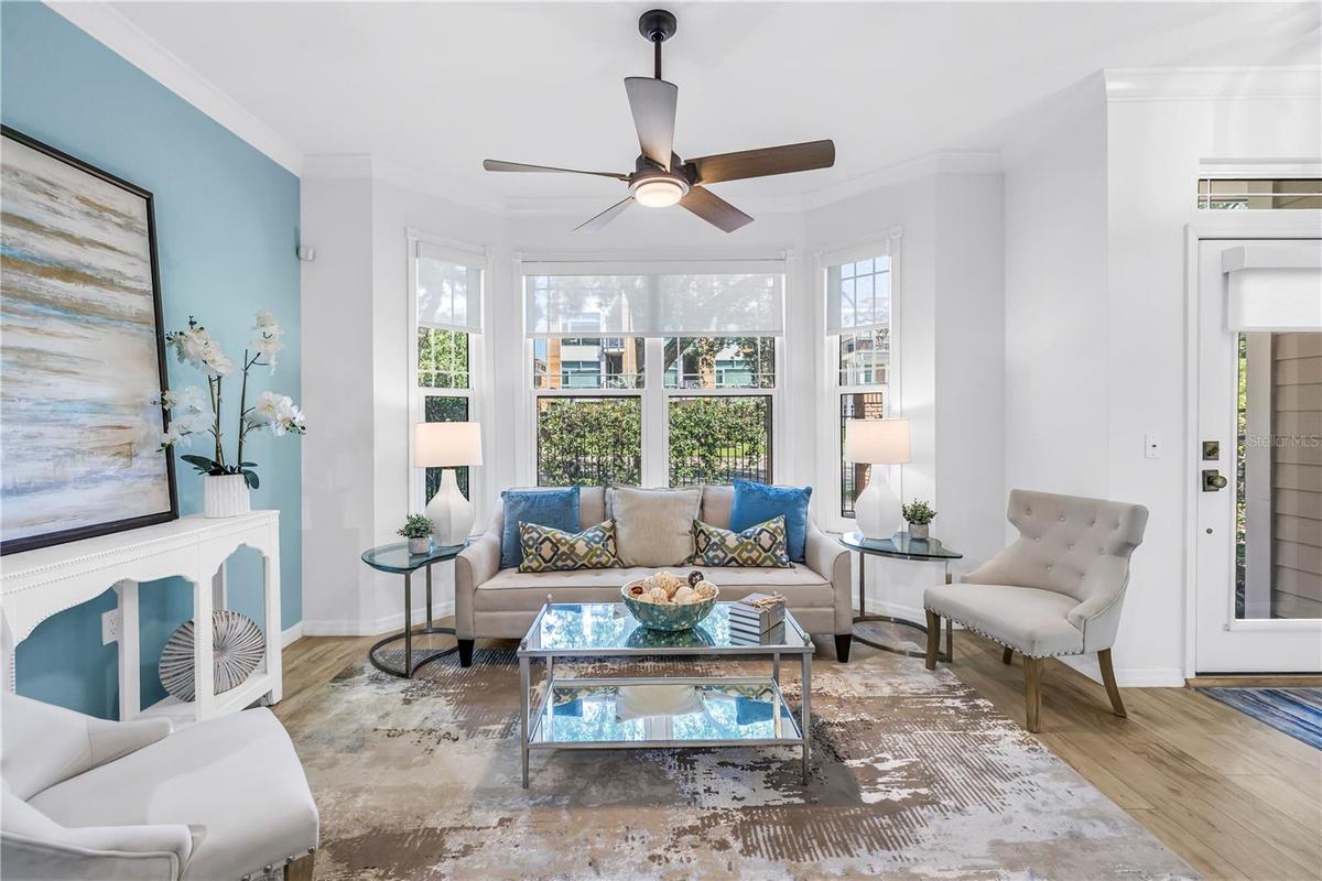 Bright and inviting living room features a bay window, luxury vinyl plank flooring and a remote-controlled sun shade.
