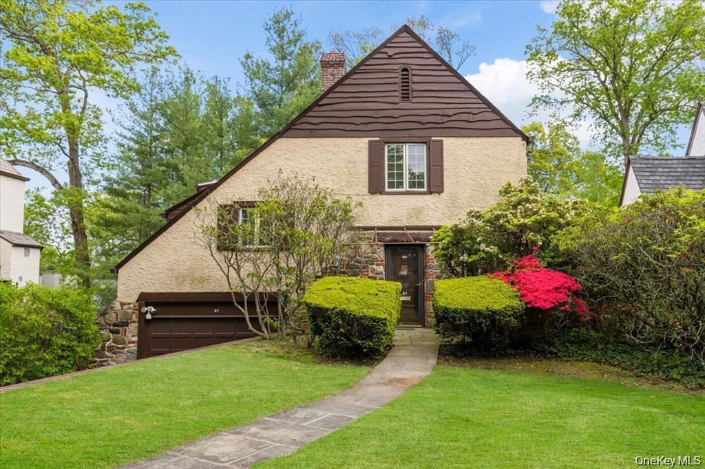 View of front of property with a chimney, stone siding, a front yard, and stucco siding