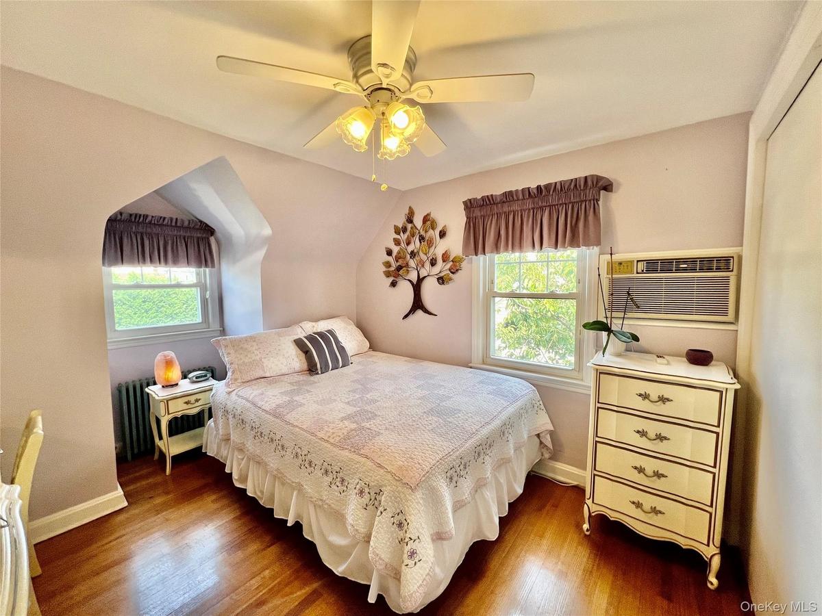Hardwood flooring, ceiling fan with integrated lighting, window with arched architectural detail, multiple windows, built-in wall air conditioning uni
