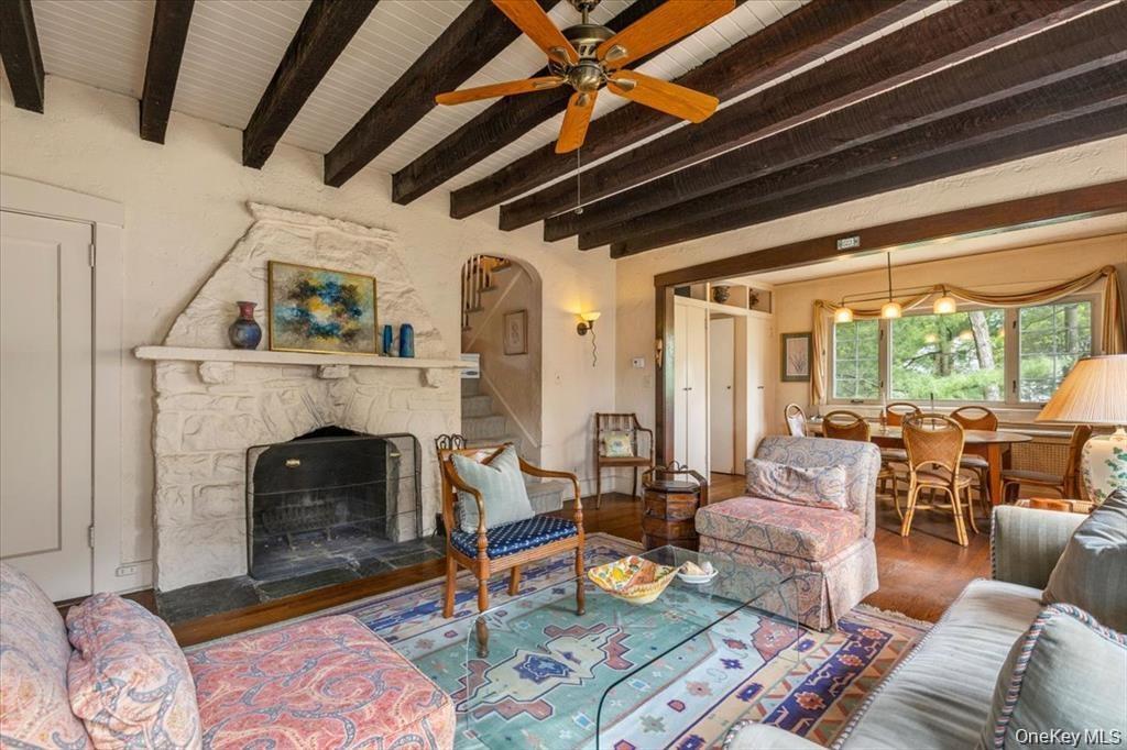 Living room with beamed ceiling, wood finished floors, a ceiling fan, a stone fireplace, and arched walkways