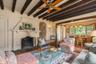 Living room with beamed ceiling, wood finished floors, a ceiling fan, a stone fireplace, and arched walkways