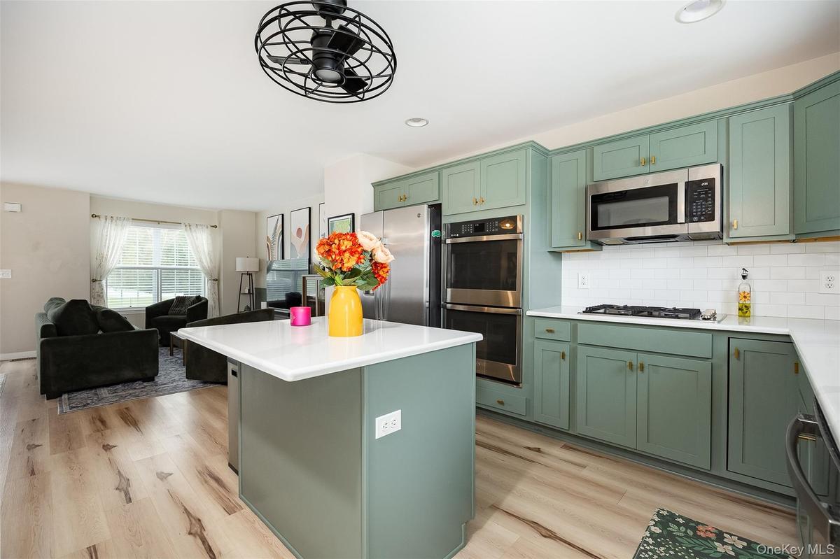 Open-concept kitchen with sage green cabinetry, stainless steel appliances, white subway tile backsplash, and a central island with a white countertop