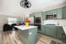 Open-concept kitchen with sage green cabinetry, stainless steel appliances, white subway tile backsplash, and a central island with a white countertop