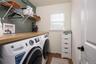 Laundry room with light wood-finish countertop, window with blinds, wire shelving, and a white paneled door with black hardware