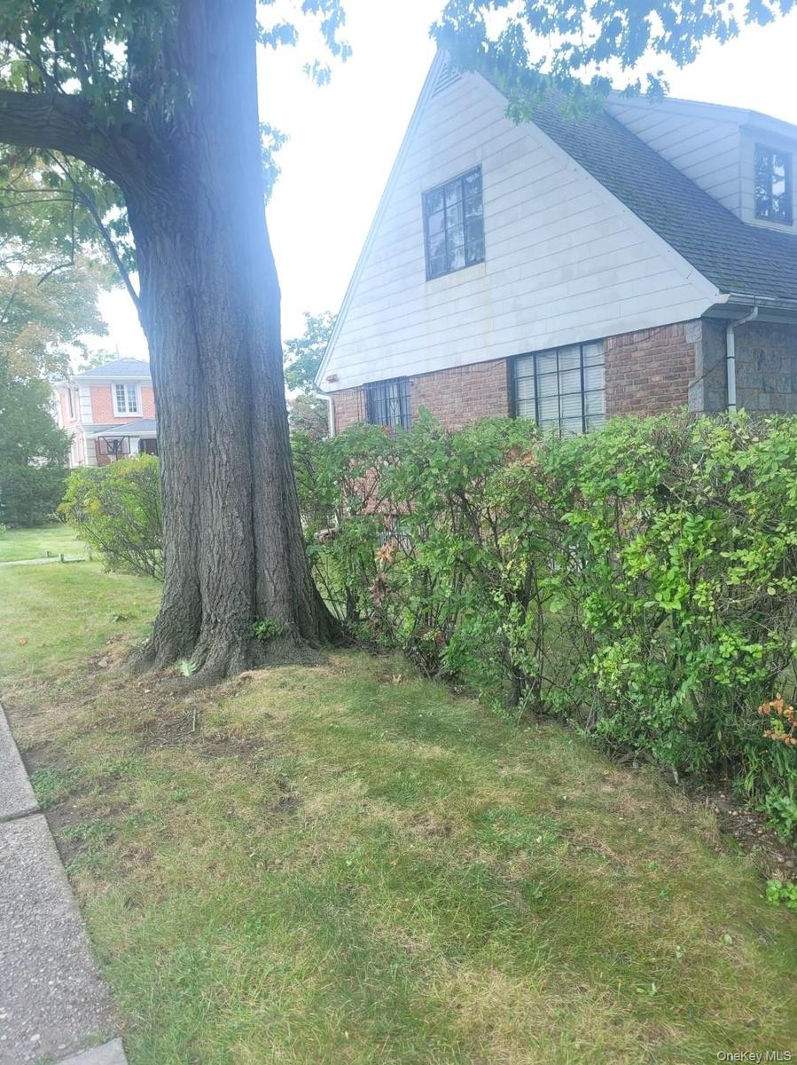 Gable roofline with dormer window, brick and siding exterior, established tree, and sidewalk access