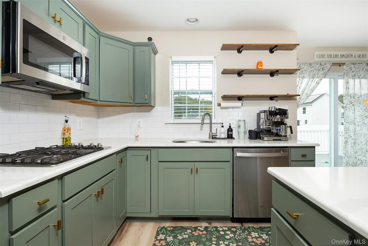 Green shaker-style cabinetry with gold-tone hardware, white countertops, stainless steel appliances, and subway tile backsplash