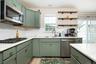 Green shaker-style cabinetry with gold-tone hardware, white countertops, stainless steel appliances, and subway tile backsplash