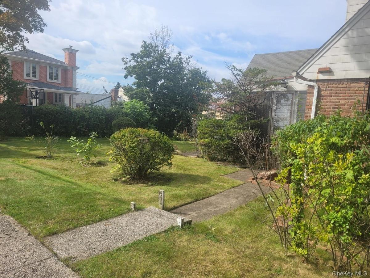 Manicured lawn with mature shrubs and trees, featuring a concrete pathway