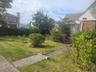 Manicured lawn with mature shrubs and trees, featuring a concrete pathway