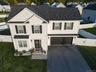 White siding with black shutters, dark shingle roof, two-car garage, paved driveway, and a white picket fence