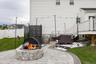 Stone-clad fire pit, paver patio, string lighting, white vinyl fencing, and white siding