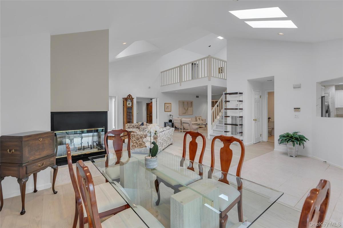 Dining area featuring a glass tabletop, a black-framed fireplace, vaulted ceilings, skylights and a partial view of a staircase with a wood railing.