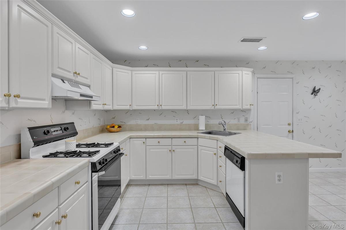 Kitchen featuring a tiled countertop, integrated dishwasher, white cabinetry, and recessed lighting. Access to the two-car attached garage.