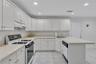 Kitchen featuring a tiled countertop, integrated dishwasher, white cabinetry, and recessed lighting. Access to the two-car attached garage.