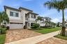 Modern architectural exterior with a stucco and stone facade, two-car garage, paver driveway, and mature landscaping