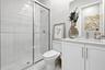 Shower with sliding glass doors, white tiled walls, white vanity with integrated sink, chrome faucet, and white cabinetry