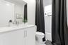 White vanity with integrated sink, chrome faucet, white countertop, white toilet, and white tiled shower surround