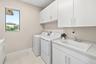 White shaker-style cabinetry with chrome hardware, an integrated laundry sink, light-toned countertop, and light-colored tile flooring
