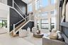 Two-story living area with high ceilings, multiple large windows, a built-in shelving unit, and a prominent staircase with wood-finish treads and an o
