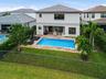 Two-story stucco exterior with a tile roof, featuring a private swimming pool, paver patio, and a fenced lawn