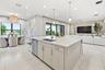 Open-concept interior featuring large format tile flooring, a kitchen island with sink and integrated dishwasher, and a dining area with expansive win