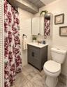 Wavy-textured wall tile, gray vanity with double cabinet doors, integrated sink, mirrored medicine cabinet, and large-format tile flooring