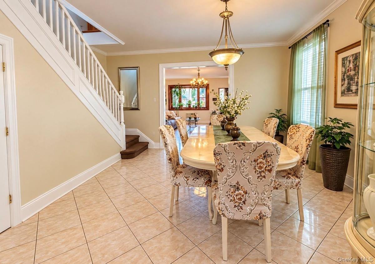 Tiled flooring, white painted staircase, recessed wall mirror, and a classic chandelier