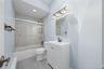 Sliding glass shower enclosure, white vanity with integrated sink, rectangular mirror, three-light vanity fixture, and recessed ceiling lighting
