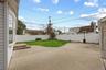 Concrete patio area with a manicured lawn section and white privacy fencing