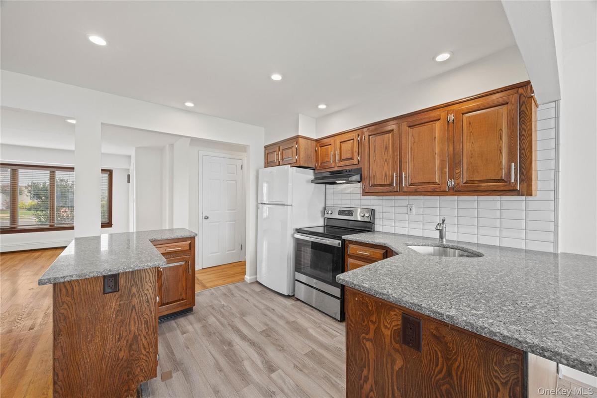 Kitchen featuring wood cabinetry, light-colored countertops, stainless steel appliances, and a tiled backsplash