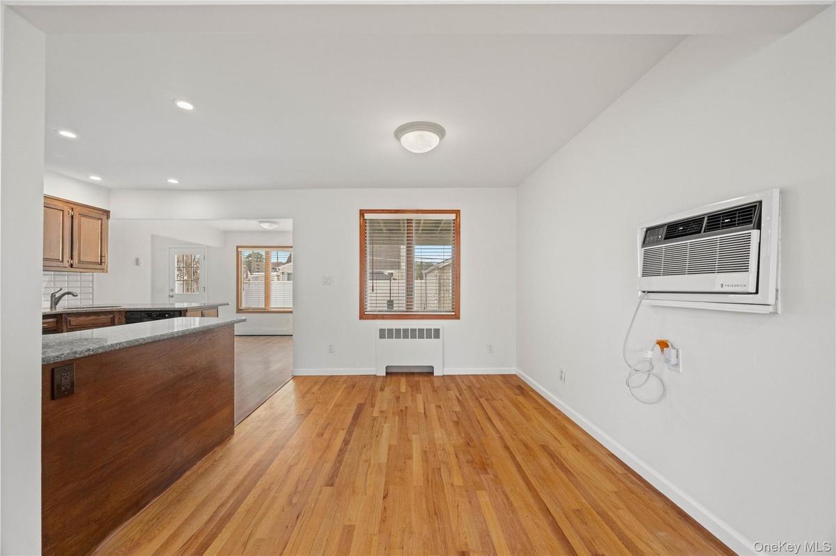 Hardwood flooring, recessed lighting, kitchen peninsula with granite countertop, wood cabinetry, and a wall-mounted air conditioning unit