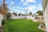 Expansive lawn with a white privacy fence, detached garage, concrete patio, and stone landscape borders