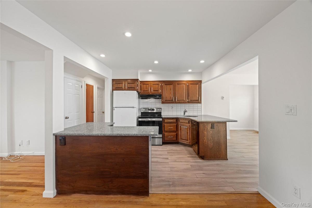 Kitchen featuring wood cabinetry, stainless steel range, white subway tile backsplash, and light-toned wood-finish flooring