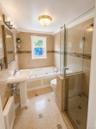 Tiled bathroom featuring a pedestal sink, jetted tub, and a glass-enclosed shower with tiled walls and floor