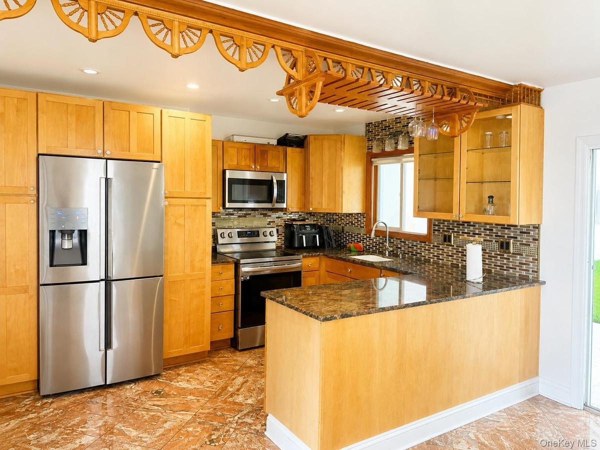 Kitchen featuring wood-finish cabinetry, stainless steel appliances, a mosaic tile backsplash, and a granite-style countertop