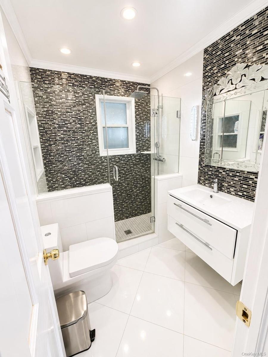 Full glass shower enclosure with a rain shower head, mosaic tiled shower walls, recessed shower shelving, and a floating vanity with a vessel sink