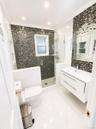 Full glass shower enclosure with a rain shower head, mosaic tiled shower walls, recessed shower shelving, and a floating vanity with a vessel sink
