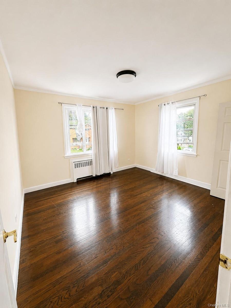 Wood-finish flooring, two windows, radiator, and a flush mount ceiling light fixture