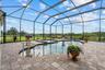 The pool deck is covered in brick paver, bronze colored pool screen and views of the back pastures