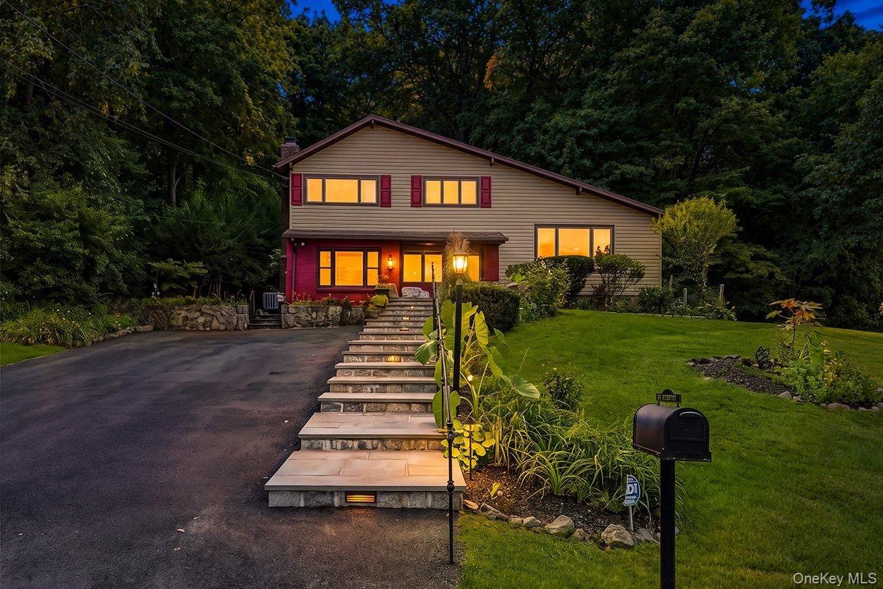 Split-level residence featuring a paved driveway, stone retaining walls, and a multi-level stone walkway.