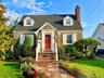 Stone exterior with white shutters, a red front door, dormer windows, a brick chimney, and a stone-paver walkway