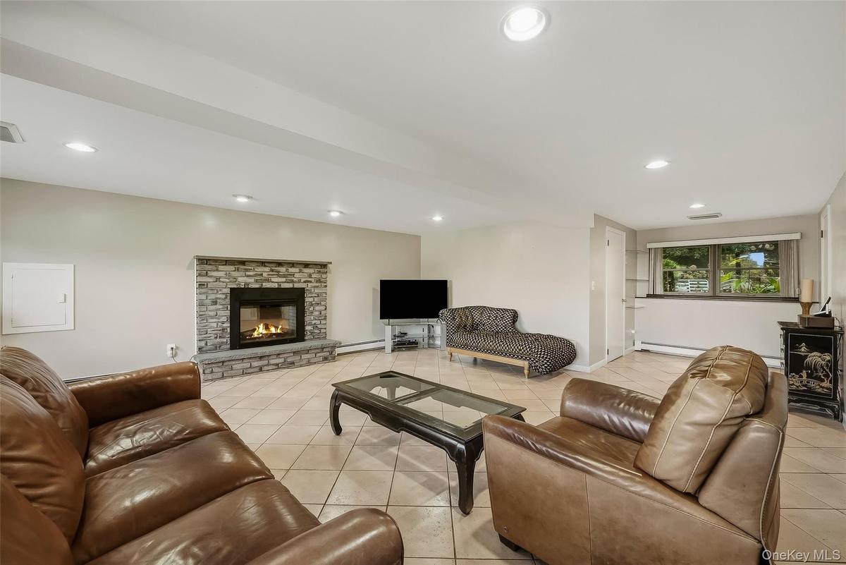 Tile flooring, stone-faced fireplace with hearth, recessed lighting, and window overlooking the backyard.