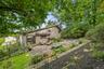 Expansive rear patio area featuring concrete paving, mature landscaping, and a tiered, mulched garden bed