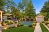 AI GENERATED PHOTOExpansive outdoor deck with dark railing, a dedicated sports court, detached garage structure, landscaped garden beds with stone ret