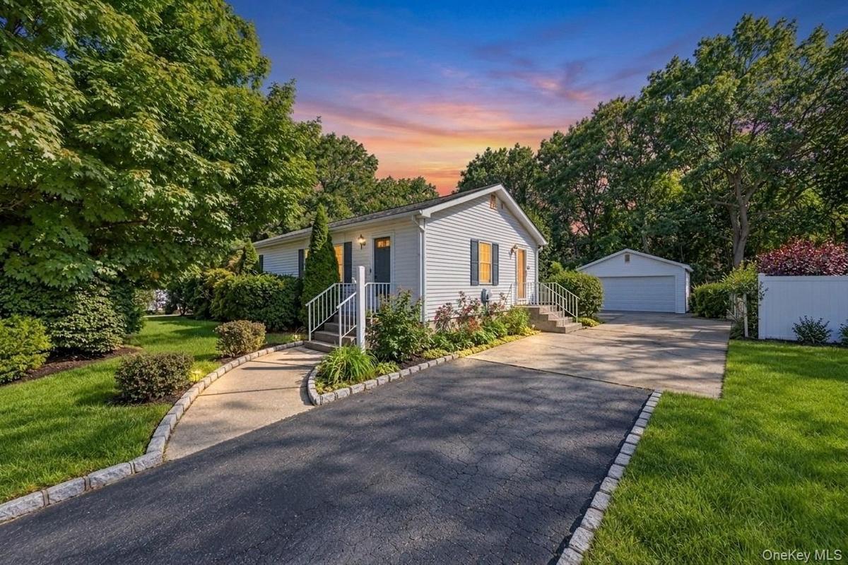 Exterior featuring siding, mature trees, a paved driveway, and a detached garage